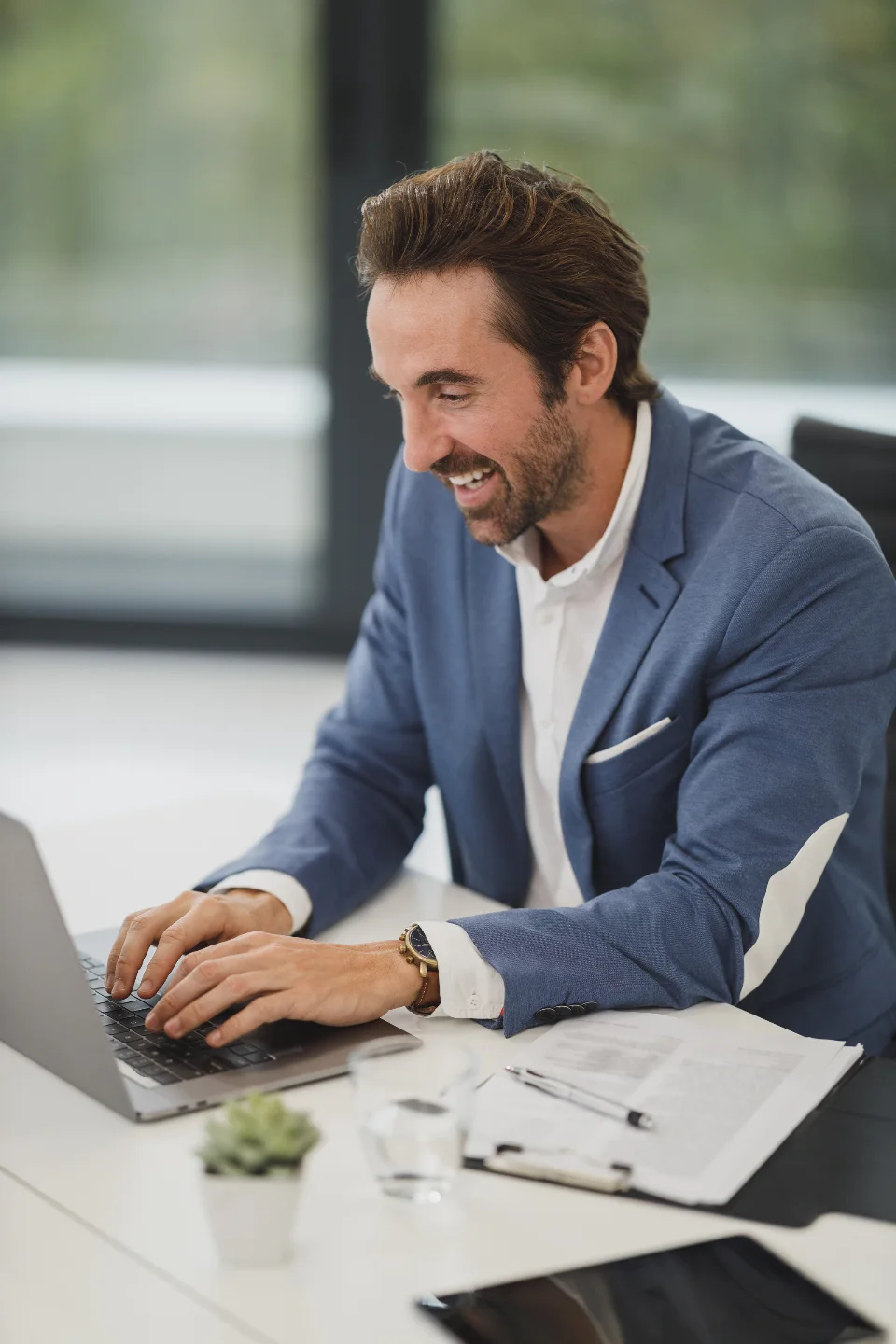 A man in a blue blazer laughing as he works on his laptop