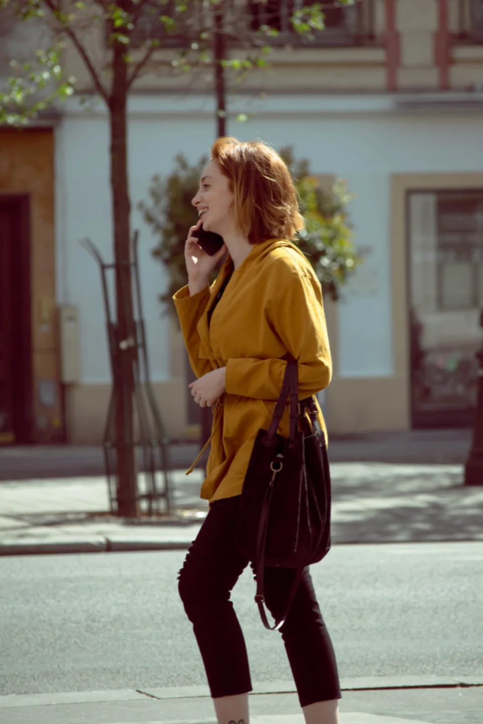 A woman on her phone walking down a sunny city street